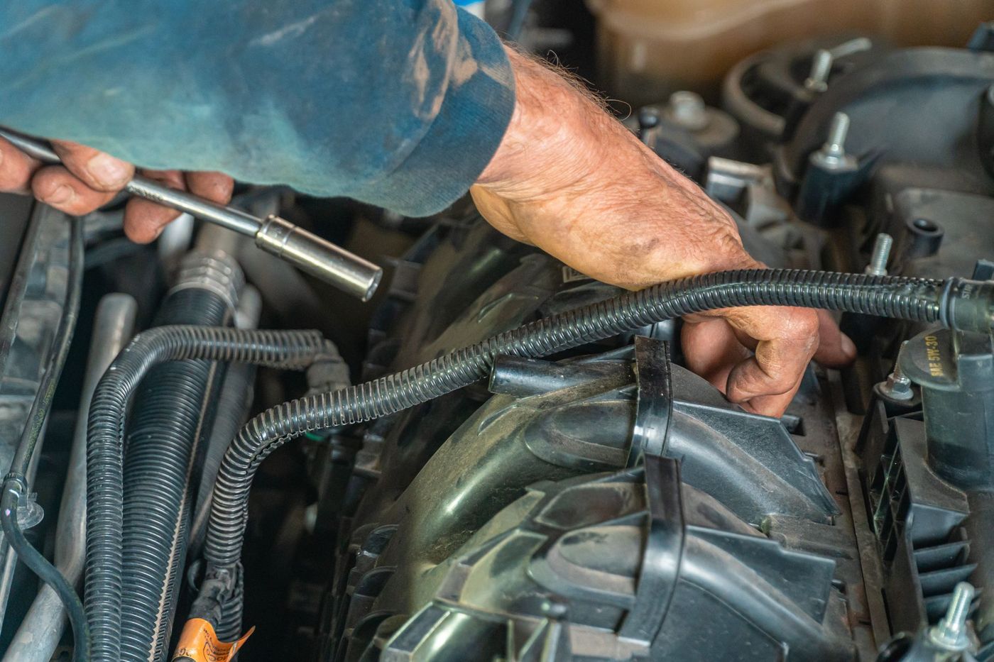 Hands using a socket wrench in an engine bay near the belt and accessory drive