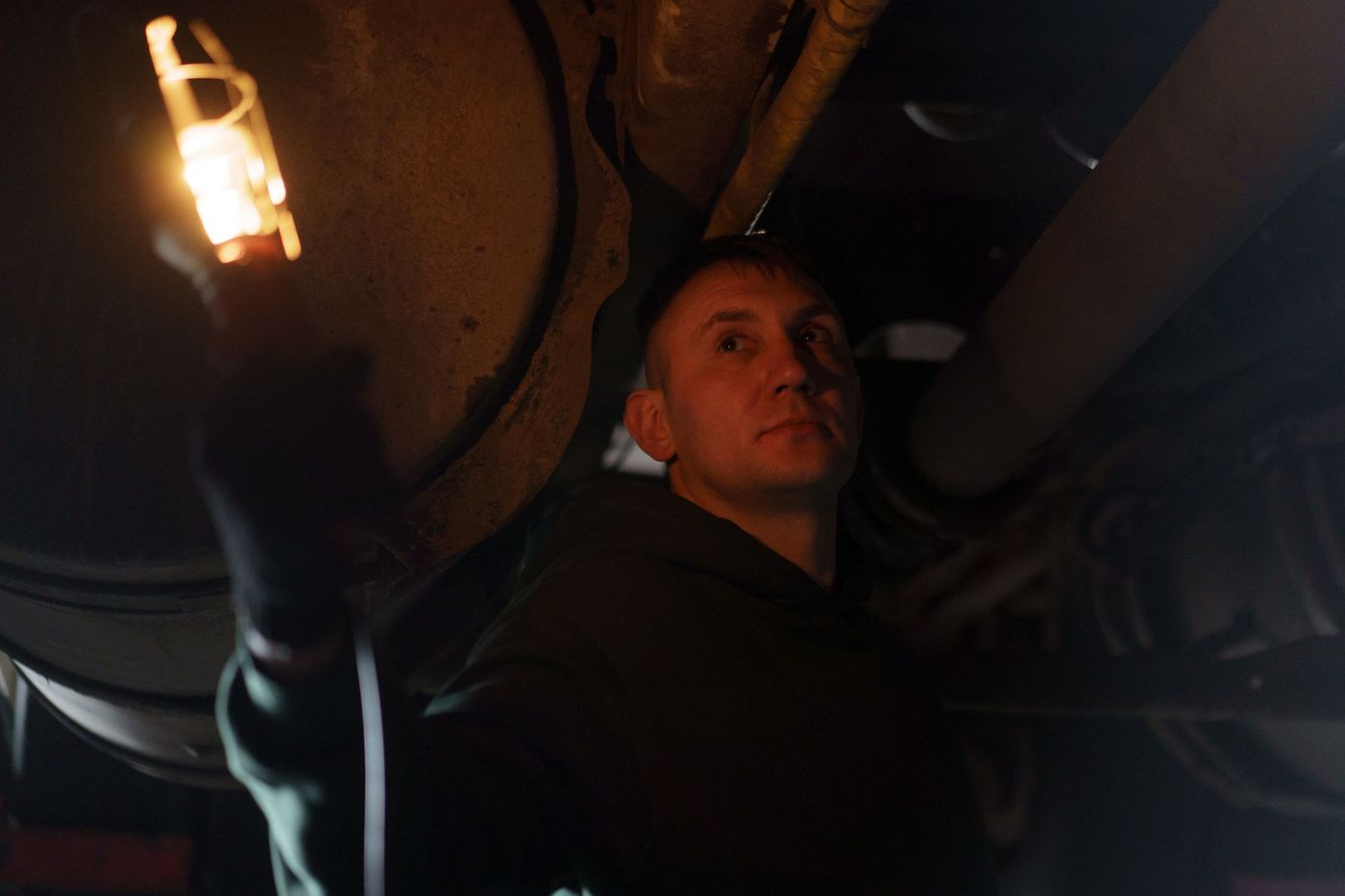 A mechanic holding an inspection lamp while working under a vehicle in near darkness