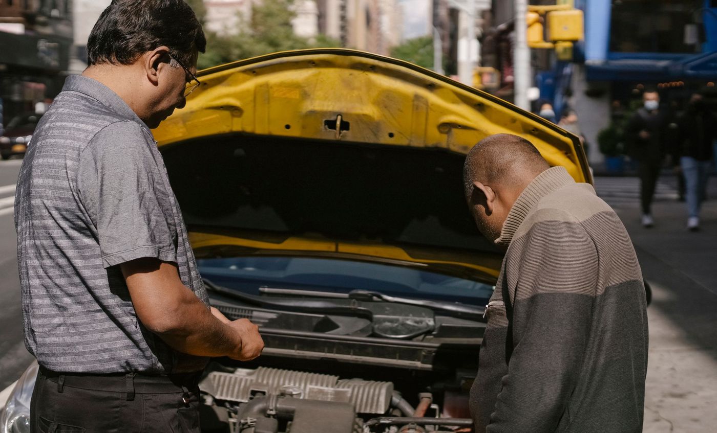 Two people diagnosing a car with its hood up at the roadside