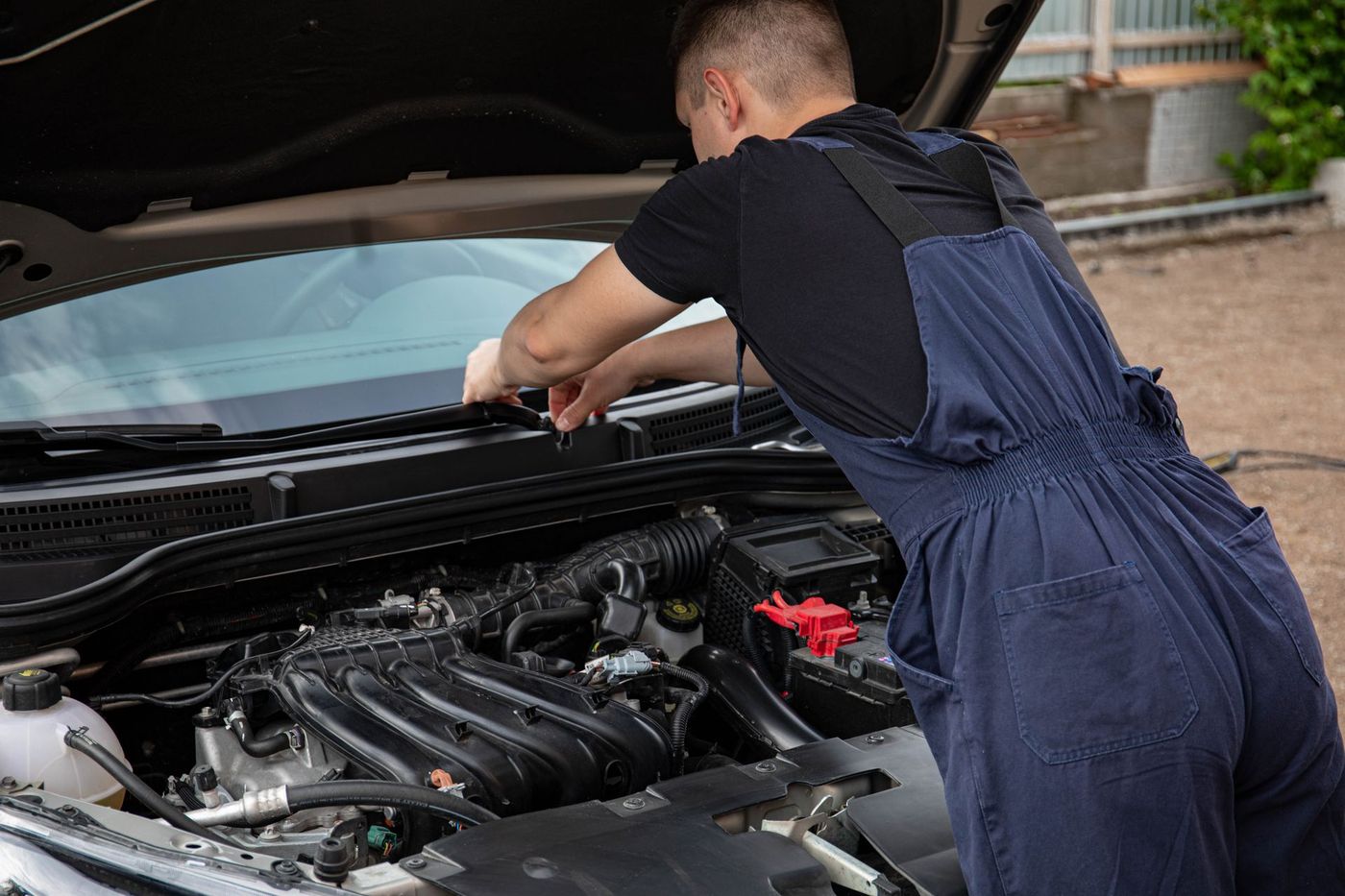 Mechanic leaning into an open hood, working outdoors on gravel